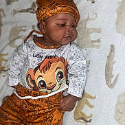 Chozyn is registered to the contest to win money with this photo: baby, child, infant, lying_down, lion_king, orange_clothing, hat, blanket, animal_print, cute, portrait, indoors, one_person, toddler, smiling, face, clothing, patterned, soft_texture, resting