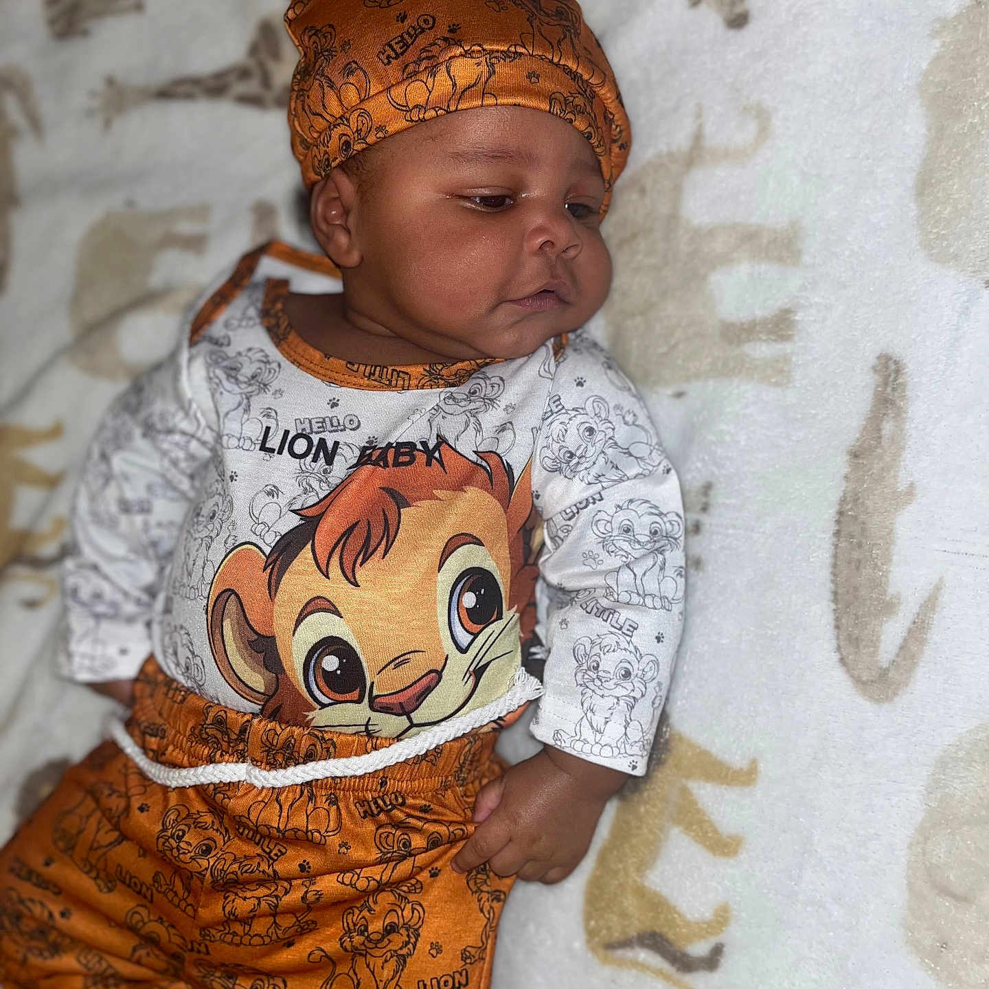 Chozyn is registered to the contest to win money with this photo: baby, child, infant, lying_down, lion_king, orange_clothing, hat, blanket, animal_print, cute, portrait, indoors, one_person, toddler, smiling, face, clothing, patterned, soft_texture, resting