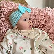 Dollie is registered to the contest to win money with this photo: baby, headband, blue_bow, pink_cushion, floral_outfit, bib, infant, soft_texture, cute, portrait, side_view, indoor, child, cozy, clothing, face, skin, person, young, comfort