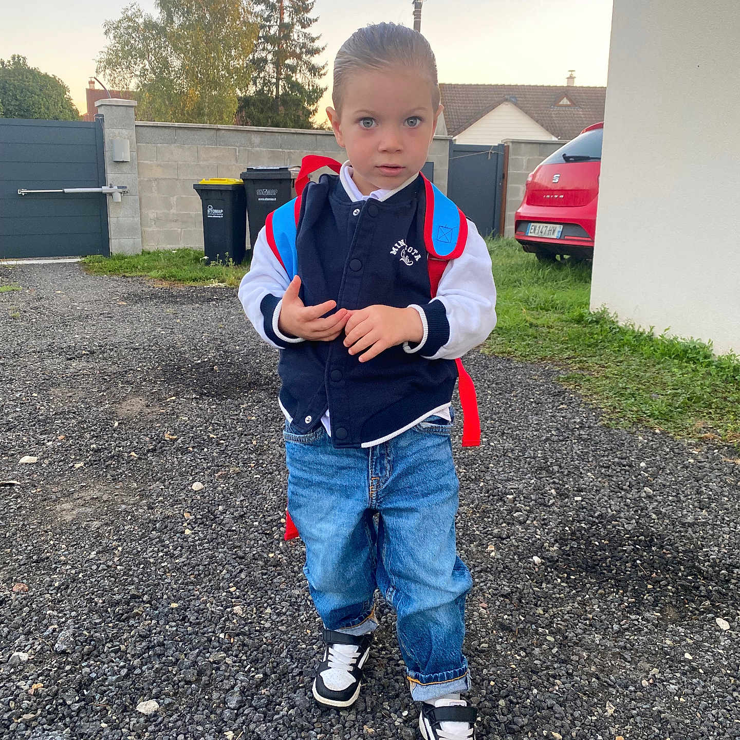 Ziane a rejoint le concours — aidez-le/la à gagner de superbes lots ! backpack, boy, car, casual_clothing, child, daylight, driveway, grass, gravel, jacket, jeans, outdoor, person, sky, sneakers, standing, suburban, trash_bins, tree, young