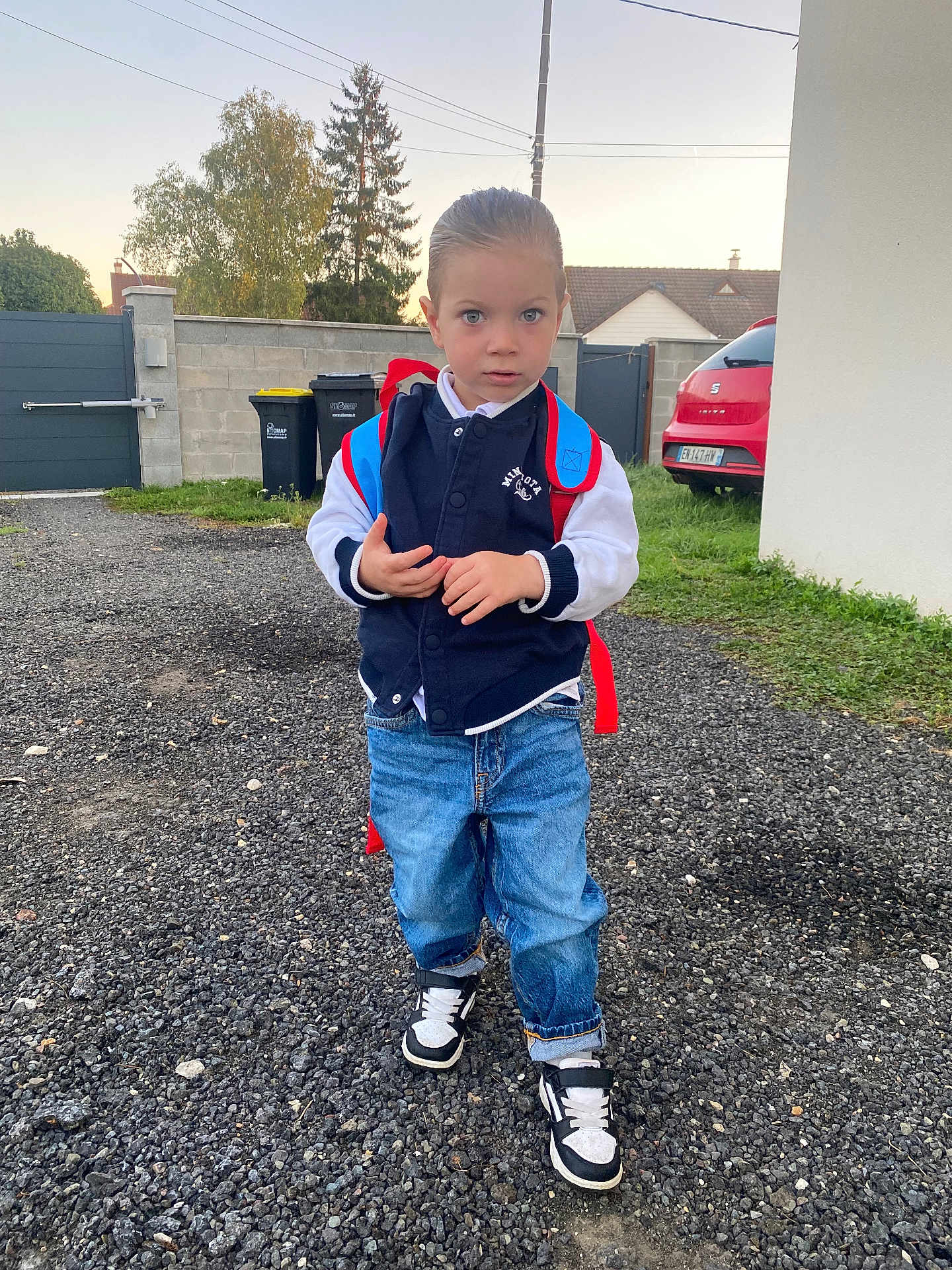 Ziane a rejoint le concours — aidez-le/la à gagner de superbes lots ! backpack, boy, car, casual_clothing, child, daylight, driveway, grass, gravel, jacket, jeans, outdoor, person, sky, sneakers, standing, suburban, trash_bins, tree, young