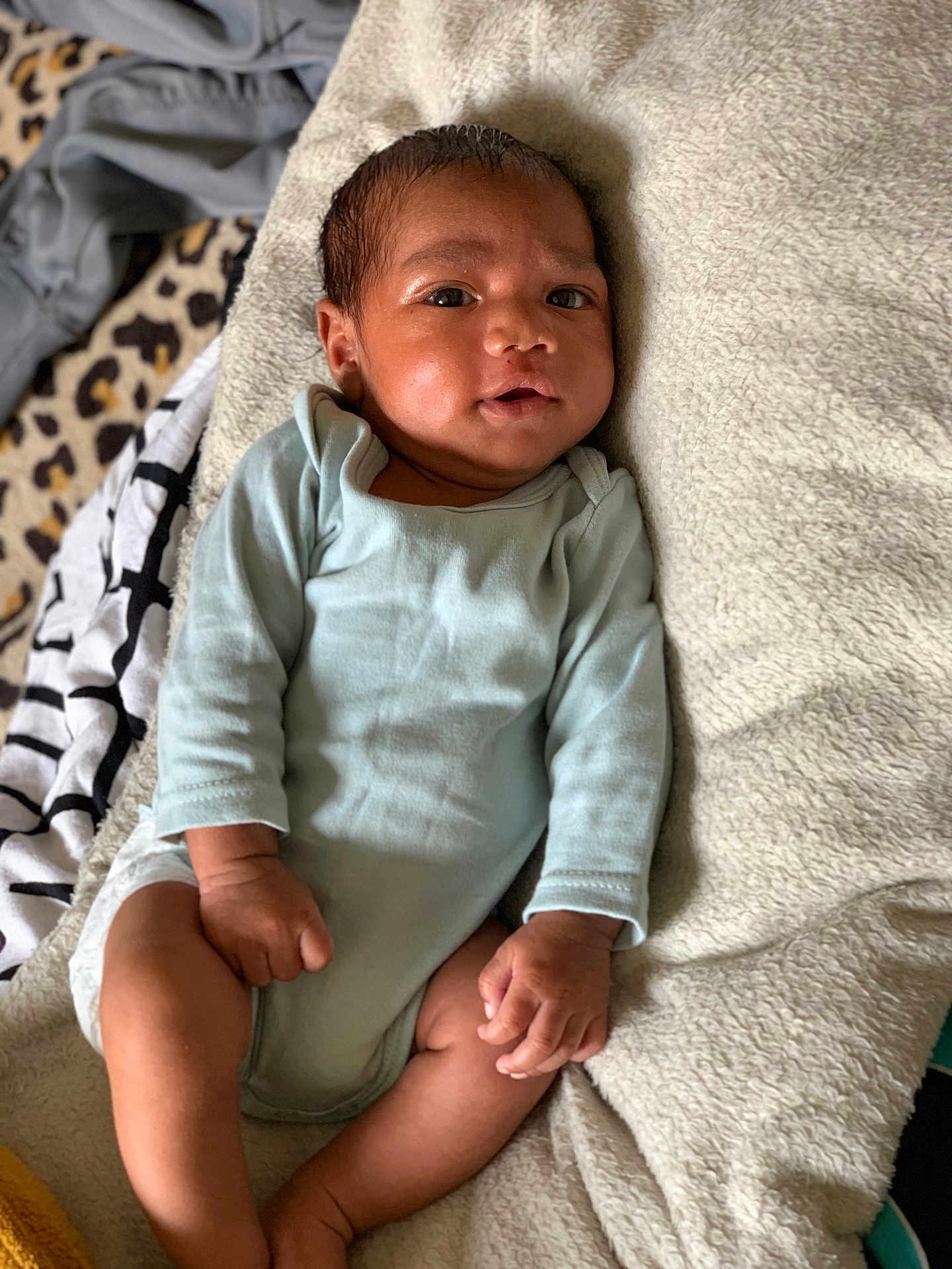 Eliézer participe au concours pour gagner de l'argent avec cette photo : baby, infant, onesie, blanket, soft_fabric, leopard_print, patterned_cloth, skin, face, hands, legs, curious_expression, lying_down, indoors, cozy, child, newborn, casual_clothing, relaxed, portrait