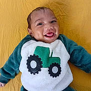 Eliézer a rejoint le concours — aidez-le/la à gagner de superbes lots ! baby, child, cozy_clothing, cute, dimples, face, green, happy, infant, lying_down, person, portrait, sleeves, smiling, soft_texture, tongue_out, tractor, white, yellow_background, young_child