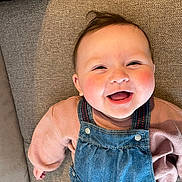 Emy participe au concours pour gagner de l'argent avec cette photo : baby, clothing, couch, cute, denim_overalls, eyes, face, hair, hand, happy, infant, joyful, laughing, mouth_open, pink_sweater, portrait, rosy_cheeks, skin, smiling, upholstery