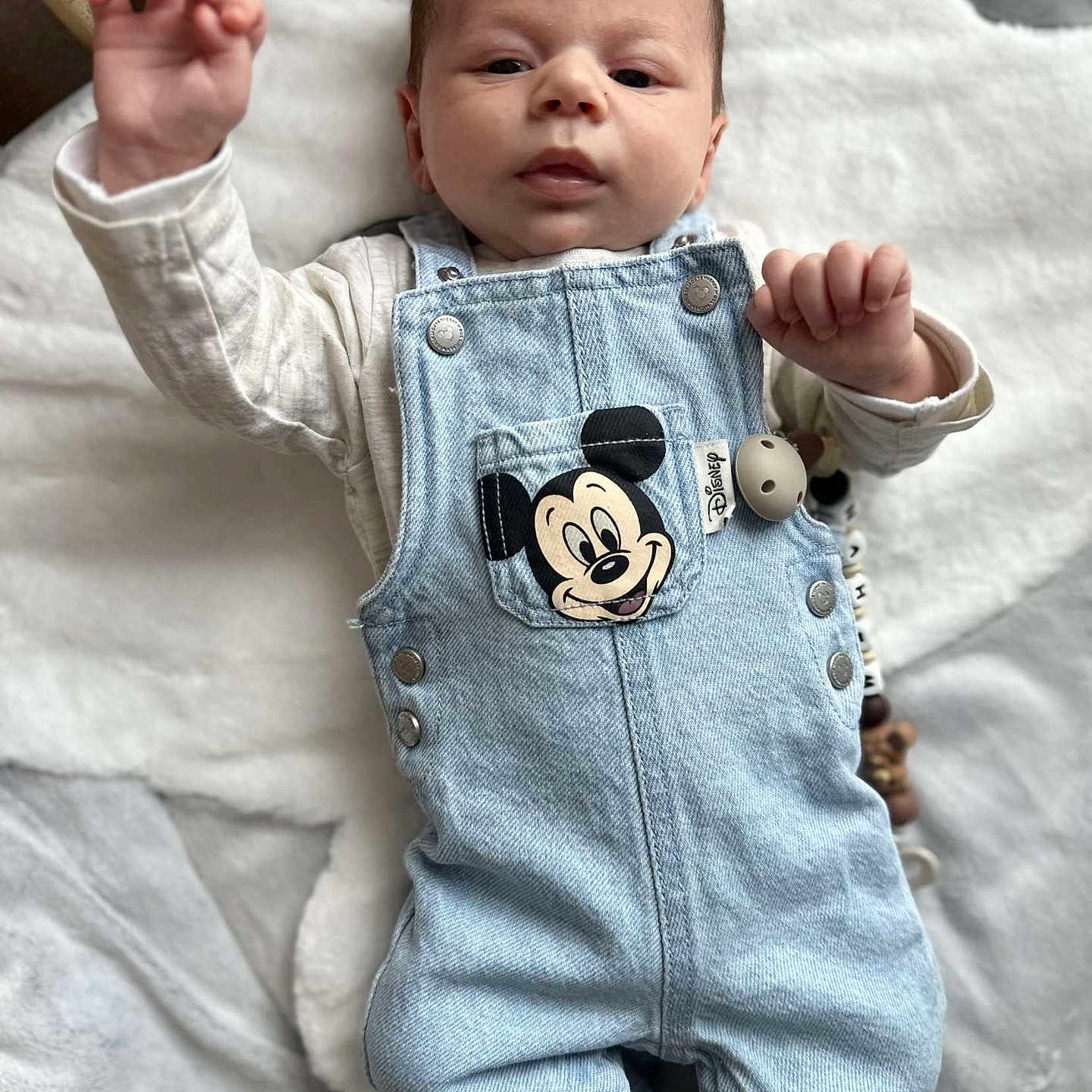 Nahim a rejoint le concours — aidez-le/la à gagner de superbes lots ! baby, bed, blanket, cartoon, casual, child, clothing, cute, denim_overalls, expression, face, hand, indoors, infant, lying_down, mickey_mouse, person, portrait, raised_hand, soft_texture