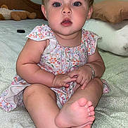 Blakeley is registered to the contest to win money with this photo: baby, child, infant, sitting, bed, floral_dress, bows, hair_accessory, barefoot, cute, indoors, pillow, stuffed_animal, bracelet, curious, face, skin, person, young, portrait