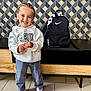 child, smiling, indoor, hoodie, jeans, sneakers, backpack, nike, braided_hair, floor_tiles, wooden_furniture, patterned_wall, standing, happy, casual_clothing, person, portrait, young_child, fashion, modern_interior