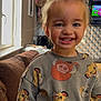 child, toddler, smiling, sweatshirt, lion_king, indoor, living_room, patterned_wallpaper, television, window, couch, happy, person, clothing, young_child, casual_wear, home, cute, portrait, playful