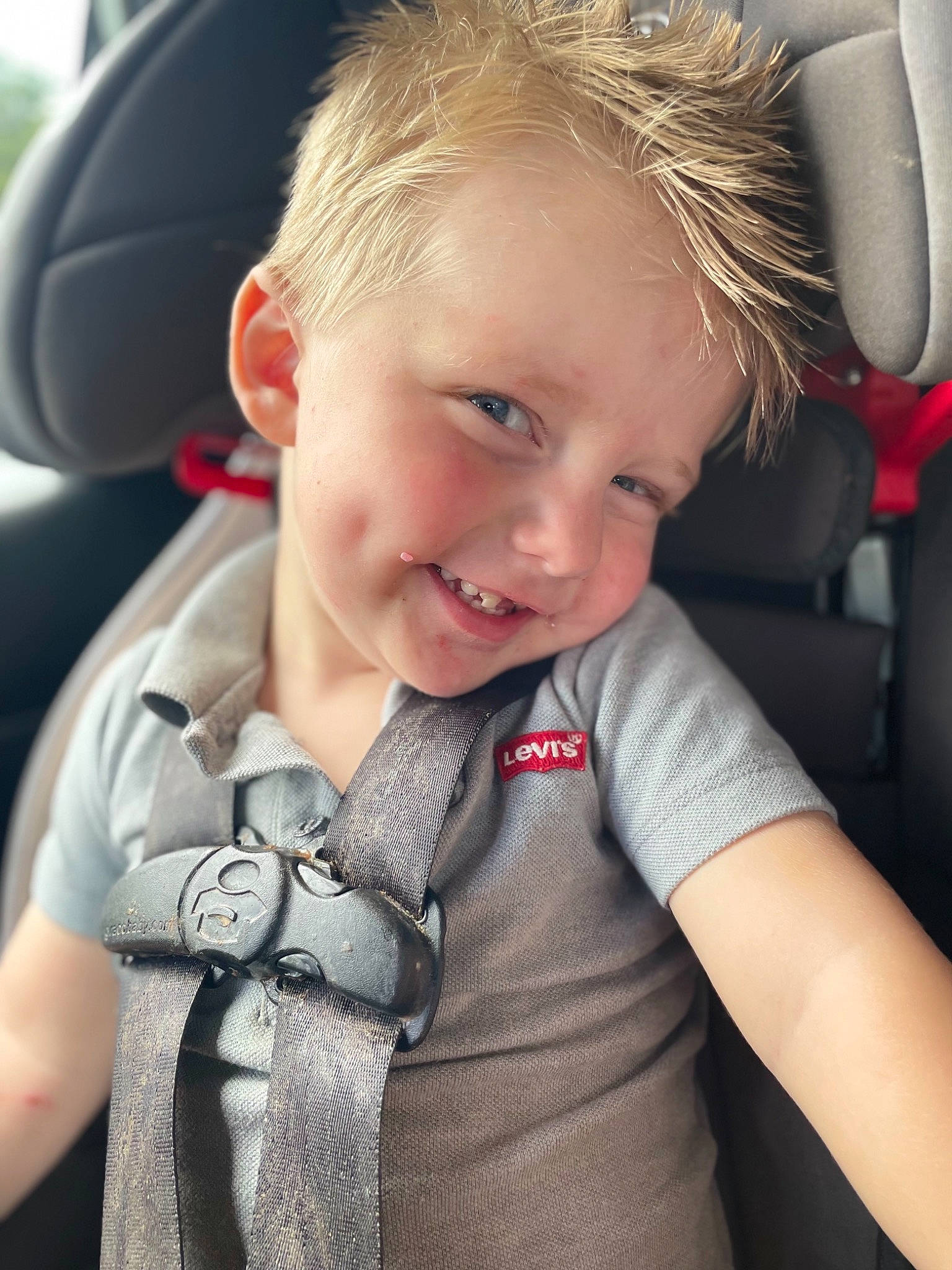 Jaxon is registered to the contest to win money with this photo: automotive_design, baby_toddler_clothing, car, car_seat, car_seat_cover, cheek, happy, head_restraint, joy, motor_vehicle, person, product, seat_belt, skin, sleeve, smile, steering_part, steering_wheel, t_shirt, toddler
