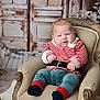 armchair, baby, blue_pants, child, chubby, cozy, cute, decorations, festive, holiday_decor, indoor, infant, portrait, red_and_white, seated, smiling, socks, striped_clothing, vintage_furniture, wooden_background