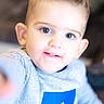 adidas_logo, baby, bokeh, candid, child, close_up, clothing, cute, eyes, face, finger_reaching, hair, happy, indoor, logo, portrait, smile, soft_lighting, sweater, toddler
