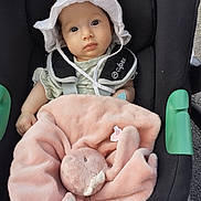 Mayna participe au concours pour gagner de l'argent avec cette photo : baby, infant, car_seat, hat, white_hat, blanket, plush_toy, bunny, pink_blanket, child, cute, seat_belt, safety_harness, outdoor, daylight, person, face, looking, baby_clothes, soft_toy