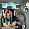 child, toddler, car_seat, car_interior, happy, smiling, baby, seatbelt, blue_shirt, foot, raised_hands, window, vehicle, headrest, seat, safety, indoor, person, casual, cute