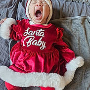 Laïana a rejoint le concours — aidez-le/la à gagner de superbes lots ! baby, blanket, child, christmas, cozy, cute, festive, fur_texture, headwear, holiday_outfit, indoors, infant, lying_down, person, red_clothing, santa_hat, sleepy, smiling, soft, yawning