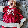 baby, blanket, child, christmas, cozy, cute, festive, fur_texture, headwear, holiday_outfit, indoors, infant, lying_down, person, red_clothing, santa_hat, sleepy, smiling, soft, yawning
