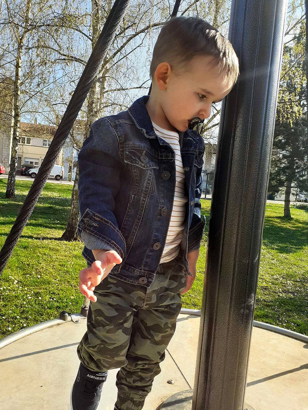 Timéo participe au concours pour gagner de l'argent avec cette photo : denim, face, grass, head, jacket, knee, leg, leisure, military_camouflage, person, plant, public_space, recreation, sleeve, sneakers, standing, street_fashion, t_shirt, toddler, tree