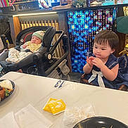 Reyna joined the competition — help win amazing prizes! baby, background, bottle, cafe, chair, child, curious, drink, food, indoor, man, napkin, person, plant, plate, restaurant, sleeping, stroller, table, toddler