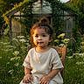 toddler, child, sitting, wooden_chair, wildflowers, garden, greenery, sunlight, outdoor, nature, topknot, white_dress, portrait, peaceful, young_child, plants, grass, flowers, daylight, cute