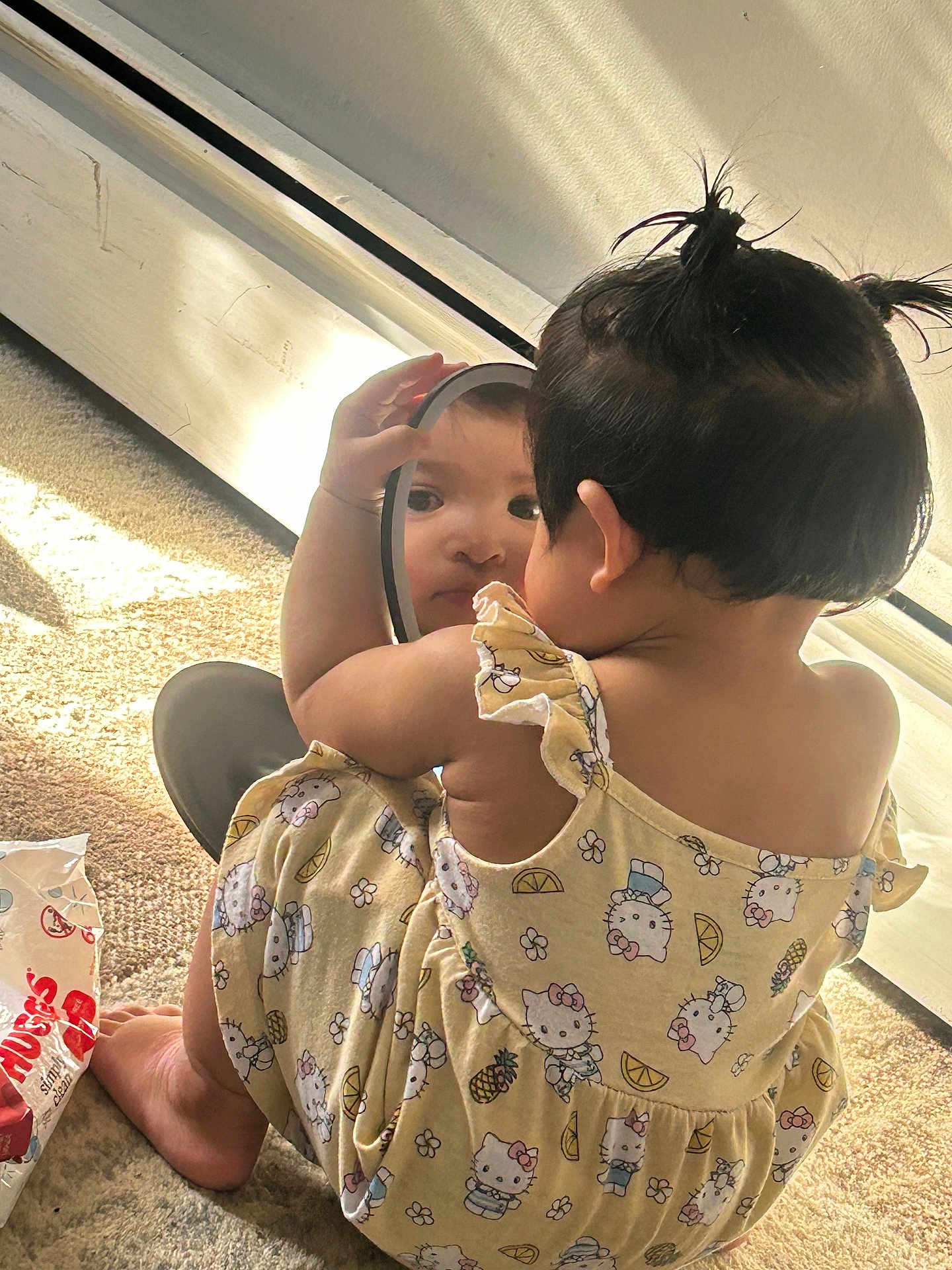 Jaylannie joined the competition — help win amazing prizes! toddler, child, mirror, reflection, yellow_dress, hello_kitty, pigtails, carpet, sunlight, indoor, baby, curious, diapers, package, window_light, cute, sitting, self_discovery, playful, home