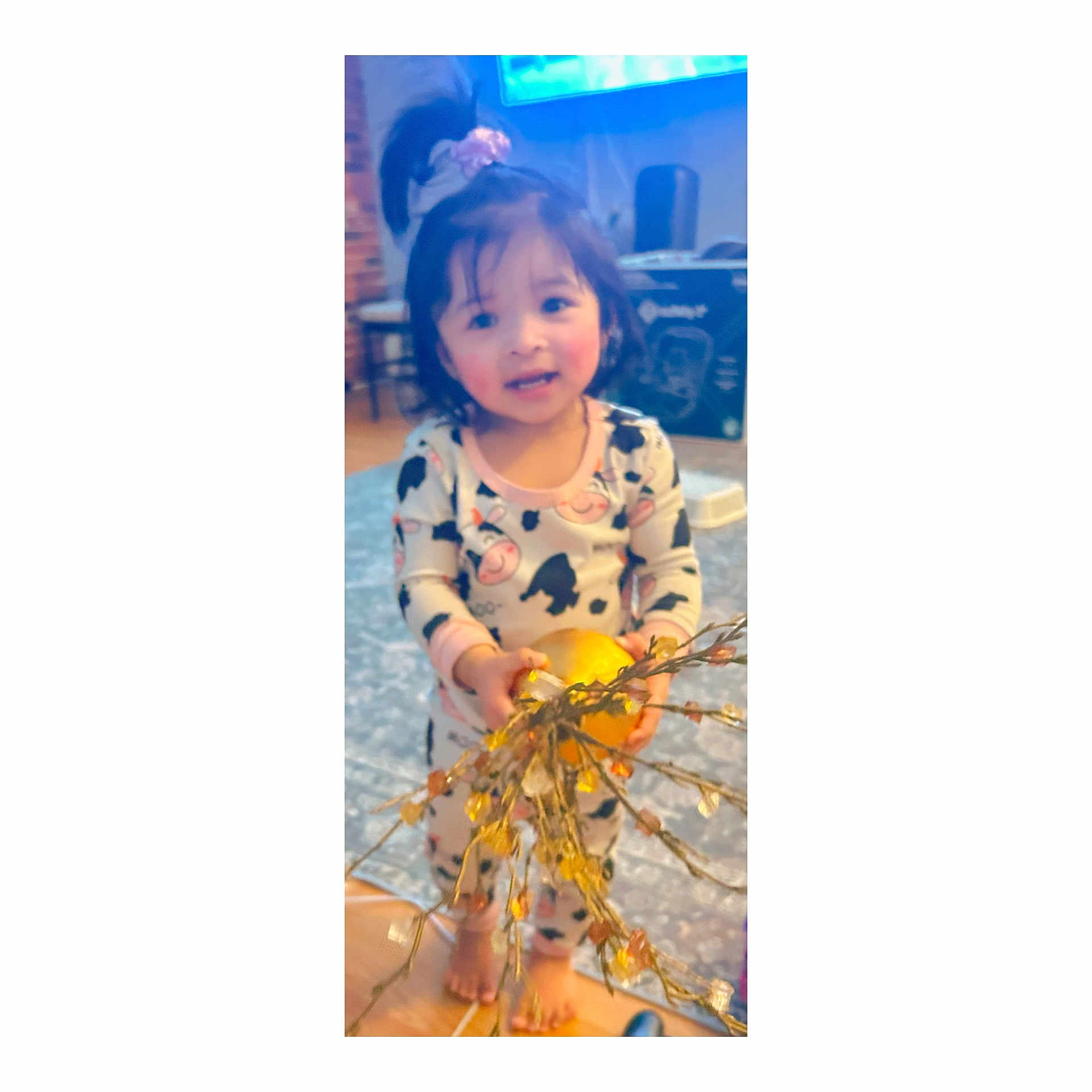 Jaylannie joined the competition — help win amazing prizes! child, toddler, pajamas, indoor, toy, orange_ball, string_lights, tv_screen, carpet, smile, face, ponytail, bare_feet, living_room, blurry, rug, cute, holding, standing, home
