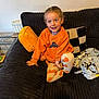 Robyn is registered to the contest to win money with this photo: child, smiling, orange_sweatshirt, pumpkin_leggings, couch, cushion, black_cushion, yellow_cushion, blanket, indoor, happy, person, home, seated, cozy, playful, casual_clothing, young_child, bright_eyes, relaxed