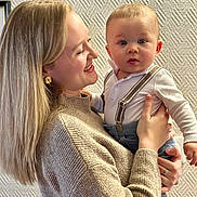 Ezio a rejoint le concours — aidez-le/la à gagner de superbes lots ! affection, baby, casual_clothing, child, closeup, curly_hair, family, framed_picture, happy, holding, home, indoor, parent, person, portrait, smiling, suspenders, sweater, wall, woman