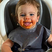 Jace is registered to the contest to win money with this photo: toddler, child, high_chair, messy_face, spaghetti_sauce, bib, smiling, kitchen, food, meal, happy, blue_eyes, curly_hair, indoor, seat, feeding, cute, small_hand, playful, young
