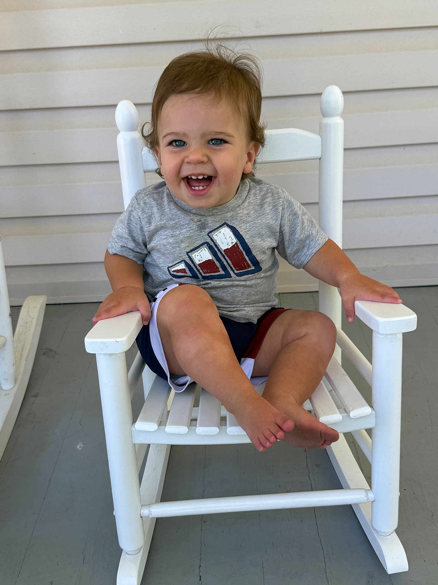 Jace is registered to the contest to win money with this photo: toddler, child, smiling, blue_eyes, gray_tshirt, shorts, rocking_chair, white_chair, porch, wooden_floor, happy, sitting, barefoot, cute, young_child, indoors, person, casual_clothing, hair, face