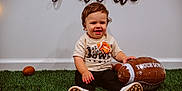 Jace is registered to the contest to win money with this photo: toddler, child, football, inflatable, grass, toy, banner, shirt, sneakers, indoor, celebration, smile, happy, playing, sport, young_child, floor, casual, cute, portrait