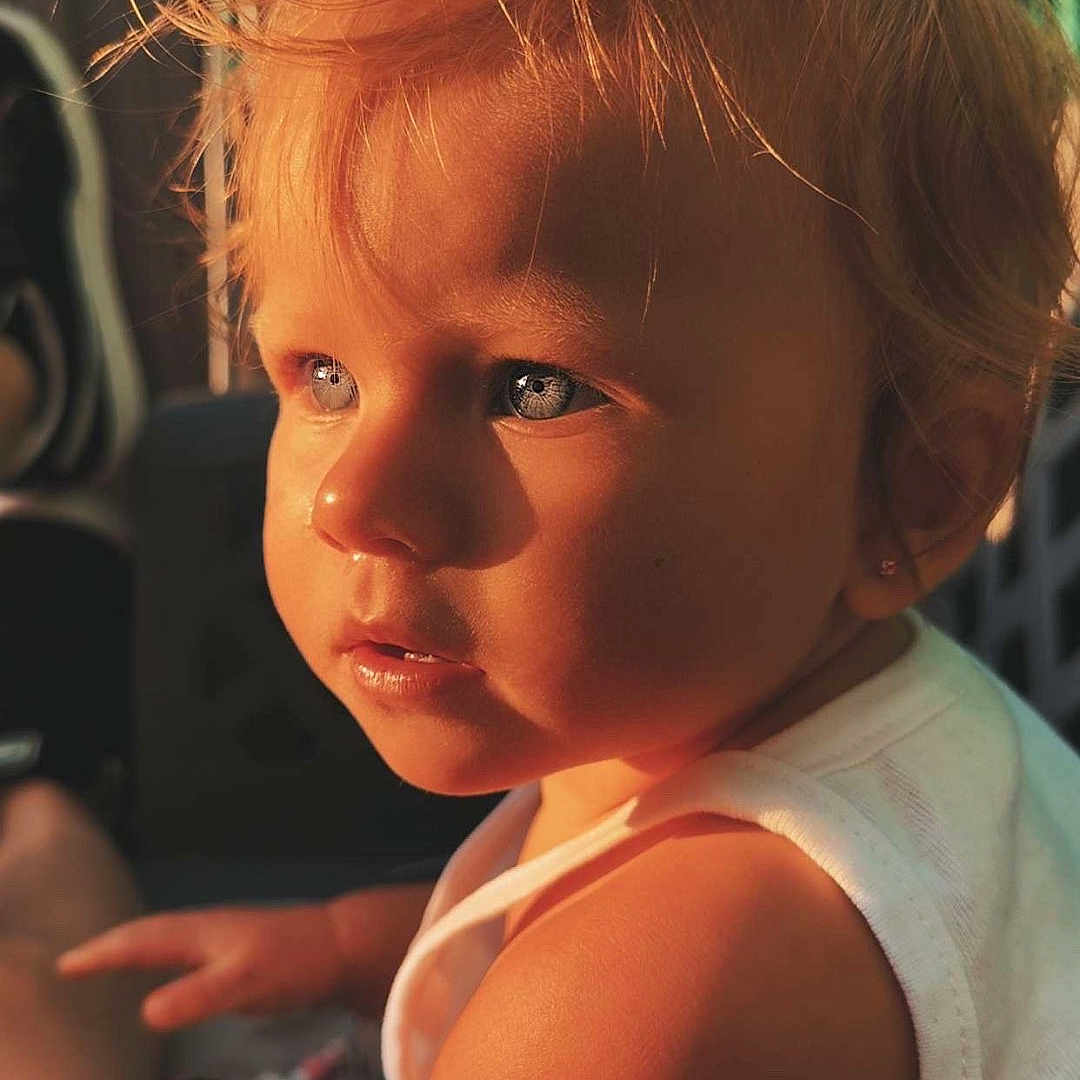 Mïa a rejoint le concours — aidez-le/la à gagner de superbes lots ! baby, blue_eyes, casual_wear, child, close_up, curious, cute, expression, face, hair, indoor, person, portrait, skin, small_earring, sunlight, toddler, warm_light, white_shirt, young_child