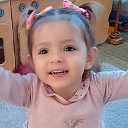 Charlotte is registered to the contest to win money with this photo: toddler, child, smiling, pink_bows, indoor, playroom, wooden_furniture, carpet, happy, cute, girl, clothing, long_sleeves, face, portrait, young_child, cheerful, baby, person, cute_expression