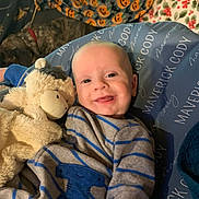 Maverick is registered to the contest to win money with this photo: baby, smiling, stuffed_animal, blue_outfit, striped_clothing, cushion, dog, blanket, pumpkin_pattern, floral_pattern, indoor, cozy, child, person, happy, cute, portrait, lying_down, pet, soft_toys