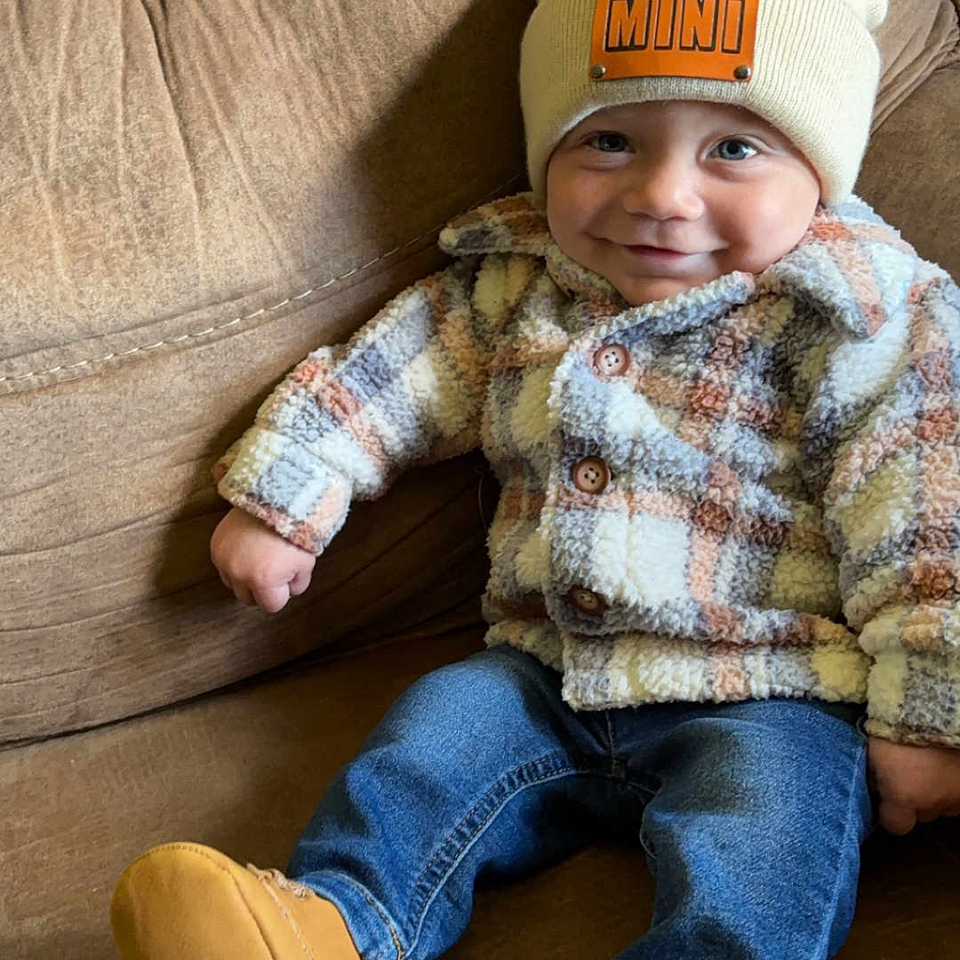 Zaydin is registered to the contest to win money with this photo: baby, cap, clothing, coat, couch, face, footwear, furniture, hat, head, jacket, jeans, knitwear, pants, person, photography, portrait, shoe, sitting, sweater
