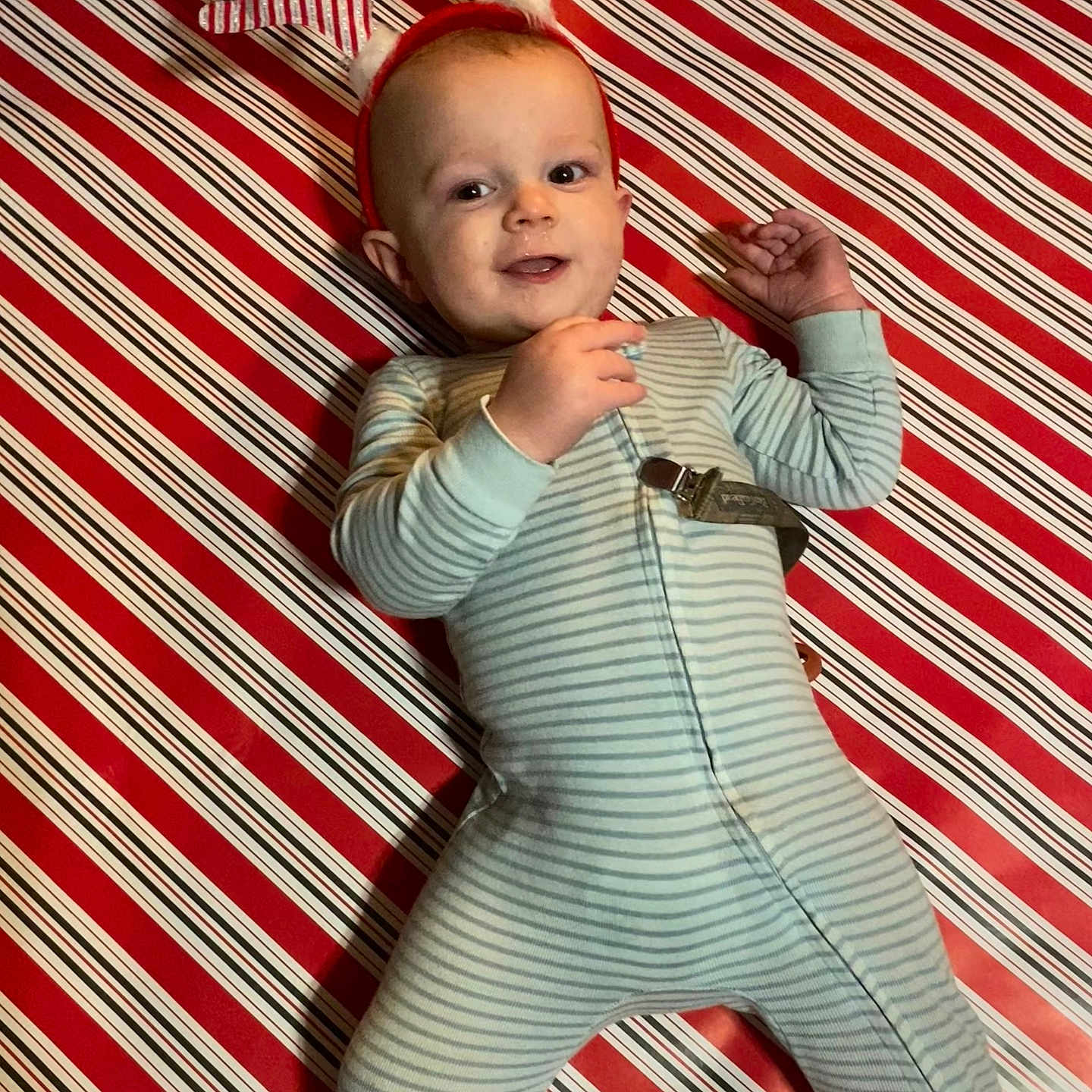 Asher joined the competition — help win amazing prizes! baby, background, celebration, child, cute, face, festive, happy, holiday, indoor, infant, lying_down, pajamas, pattern, person, red, reindeer_antlers, smiling, striped_clothing, white