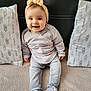 baby, child, smiling, headband, bow, sweater, hearts, jeans, shoes, leopard_print, couch, pillows, patterned_pillows, indoor, happy, seated, cute, person, infant, cozy