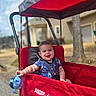 toddler, child, smiling, wagon, radio_flyer, red, blue, sippy_cup, outdoor, suburban, street, daytime, canopy, seatbelt, happy, person, baby, playful, sunny, toy