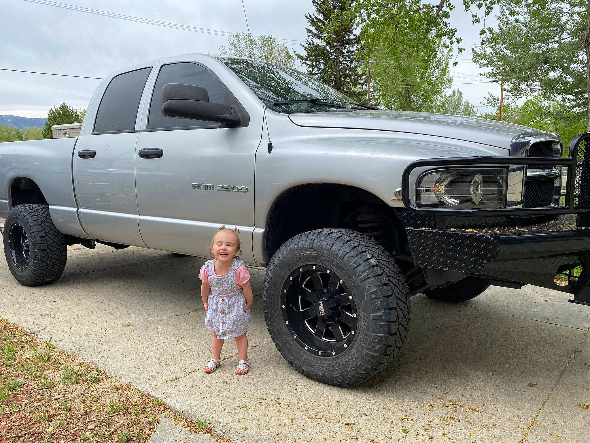 Elizabeth is registered to the contest to win money with this photo: alloy_wheel, automotive_design, automotive_exterior, automotive_lighting, automotive_tire, bumper, car, cloud, dress, hood, joy, motor_vehicle, person, rim, sky, tire, tread, tree, truck, vehicle