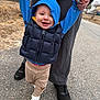 child, toddler, baby, smiling, hoodie, puffer_vest, holding_hands, adult_hands, walking, outdoor, road, pavement, grass, shoe, croc, black_shoes, pants, portrait, happy, winter_clothing