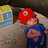 baby, newborn, infant, knitted_clothing, red_hat, blue_outfit, blanket, rocket_pattern, stars, blocks, months, cute, sleepy, indoors, soft_texture, child, small, resting, portrait, cozy