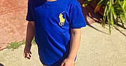 Kayden joined the competition — help win amazing prizes! child, boy, outdoor, sunlight, shadow, blue_shirt, beige_pants, white_sneakers, concrete, brick_wall, plants, smiling, standing, casual_clothing, daylight, young_child, portrait, happy, shy, nature