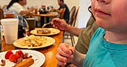 Mateo joined the competition — help win amazing prizes! blue_shirt, blurred_background, casual, child, curious, dining, drink, face, food, fork, indoor, napkin, people, plate, portrait, restaurant, seated, table, toddler, wooden_table