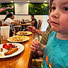 Mateo joined the competition — help win amazing prizes! child, toddler, blue_shirt, face, food, plate, table, restaurant, dining, people, indoor, blurred_background, wooden_table, fork, drink, napkin, casual, seated, curious, portrait