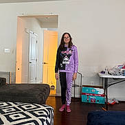 Ava is registered to the contest to win money with this photo: child, person, standing, indoor, living_room, clothing, purple, black, kuromi, glasses, door, furniture, table, box, socks, wood_floor, pattern, casual, young, smile