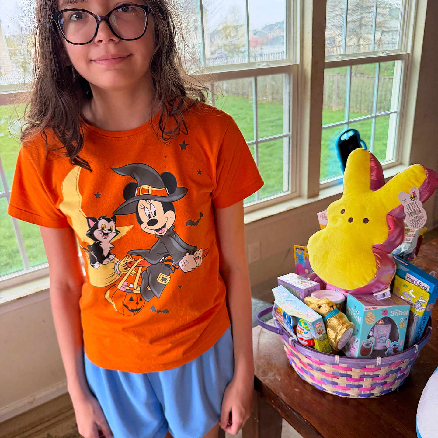 Ava joined the competition — help win amazing prizes! child, glasses, orange_tshirt, mickey_mouse, witch_costume, easter_basket, plush_toy, window, indoor, table, toys, blue_shorts, carpet, green_grass, natural_light, smile, person, holiday_theme, decor, happy
