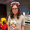 Ava is registered to the contest to win money with this photo: birthday, girl, glasses, headband, tshirt, cartoon_print, toy_car, kitchen, banner, birthday_banner, indoor, person, child, smile, long_hair, countertop, dish_rack, water_bottle, curtains, floor
