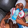 Jream is registered to the contest to win money with this photo: baby, bottle, bib, hat, person, hand, couch, diaper, child, feeding, infant, sitting, clothing, skin, closeup, indoor, parent, care, arm, comfort