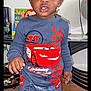toddler, child, indoor, clothing, lightning_mcqueen, blue_outfit, standing, barefoot, toy, table, globe, curly_hair, face, person, floor, car_print, pants, shirt, expression, home