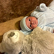 Jexiel E. is registered to the contest to win money with this photo: baby, infant, knitted_clothing, hat, teddy_bear, plush_toy, brown_rug, soft_texture, cute, child, lying_down, cozy, portrait, indoor, warm_colors, newborn, cute_face, toy, comfort, snuggle
