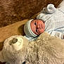 baby, infant, knitted_clothing, hat, teddy_bear, plush_toy, brown_rug, soft_texture, cute, child, lying_down, cozy, portrait, indoor, warm_colors, newborn, cute_face, toy, comfort, snuggle