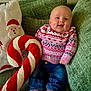 baby, child, couch, cozy, cute, festive, green_couch, happy, holiday_sweater, indoors, infant, jeans, pillow, pink_socks, pink_sweater, plush_candy_cane, portrait, santa_pillow, seated, smiling